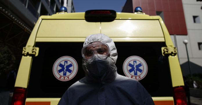 Νοσηλευτής με μαπ για covid-19 μπροστά από ασθενοφόρο