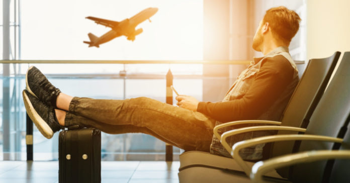 Ταξιδιώτης σε αεροδρόμιο με τα πόδια πάνω σε βαλίτσα
