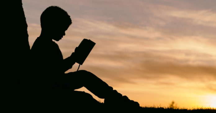 Παιδί που κάθεται και διαβάζει στο ηλιοβασίλεμα