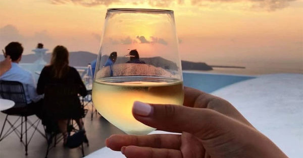 Ποτήρι κρασί με φόντο το ηλιοβασίλεμα της Σαντορίνης