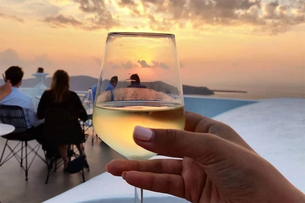 Ποτήρι κρασί με φόντο το ηλιοβασίλεμα της Σαντορίνης