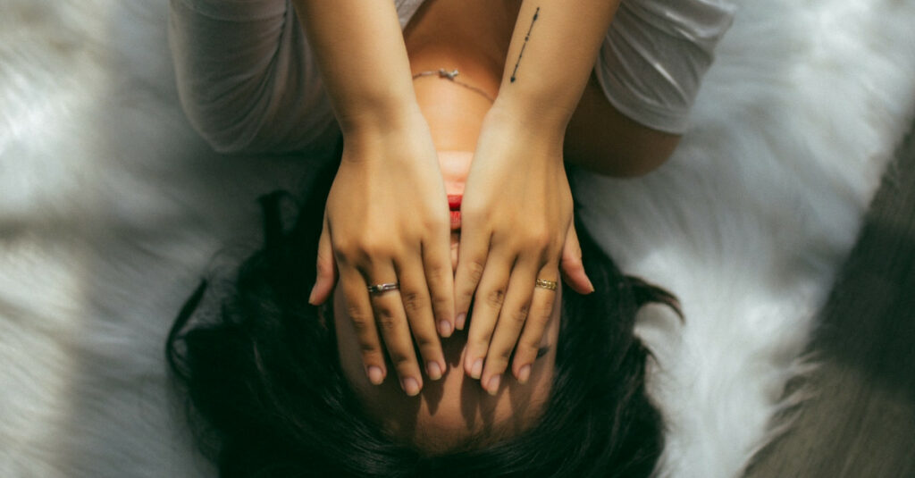 Γυναίκα σε κρεβάτι να κλείνει τα μάτια της με τα χέρια της