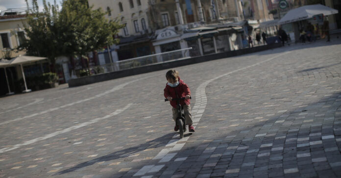 Παιδάκι με μάσκα κάνει ποδήλατο στην πλατεία στο Μοναστηράκι, άδεια από κόσμο λόγω του Lockdown