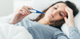 Ξαπλωμένη γυναίκα με γρίπη κοιτάει την ένδειξη του θερμόμετρου