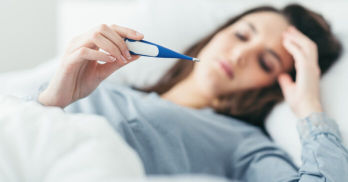 Ξαπλωμένη γυναίκα με γρίπη κοιτάει την ένδειξη του θερμόμετρου